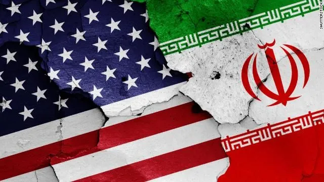 علم الولايات المتحدة وعلم إيران متداخلان على خلفية متشققة، في صورة ترمز إلى التوتر والتصعيد بين واشنطن وطهران.